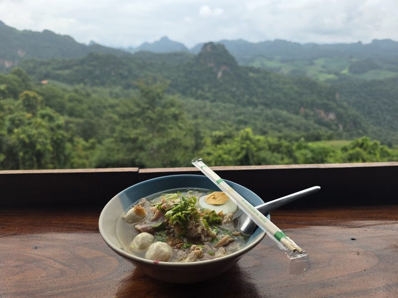 ก๋วยเตี๋ยวหนึ่งชามกับตะเกียบวางบนราวระเบียง มีทิวเขาอยู่ด้านหลัง
